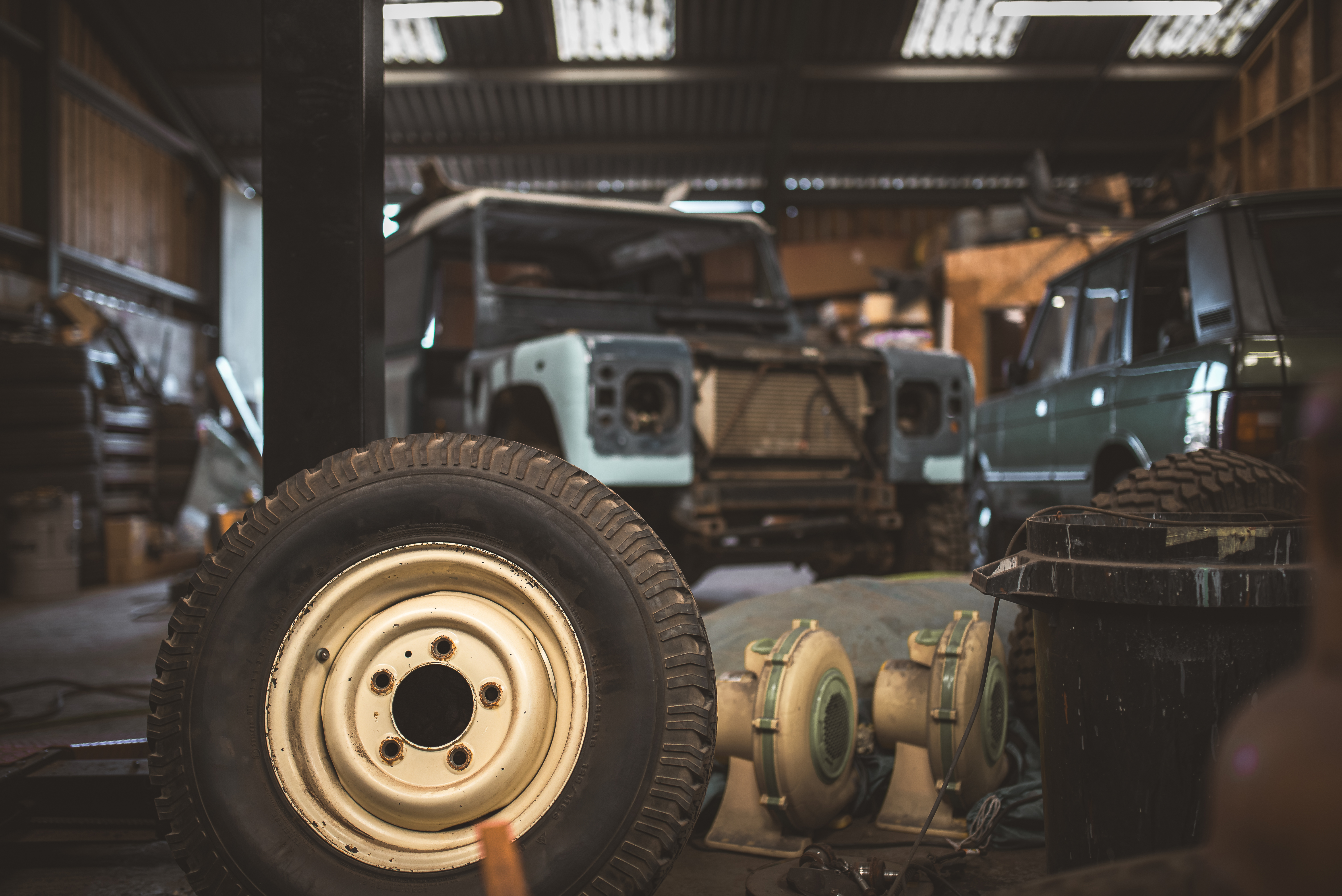 An old off road vehicle sits in a garage, surrounded by tools and parts, awaiting repairs and refurbishment